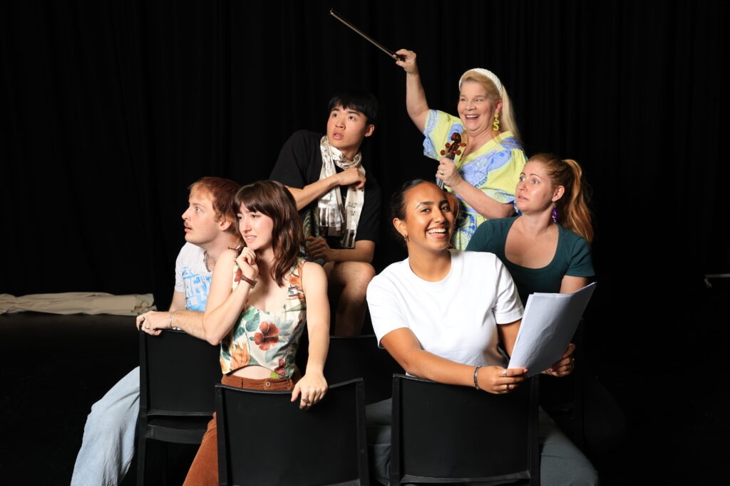 Group of six people all making different faces, one looking directly at the camera, one holding a violin